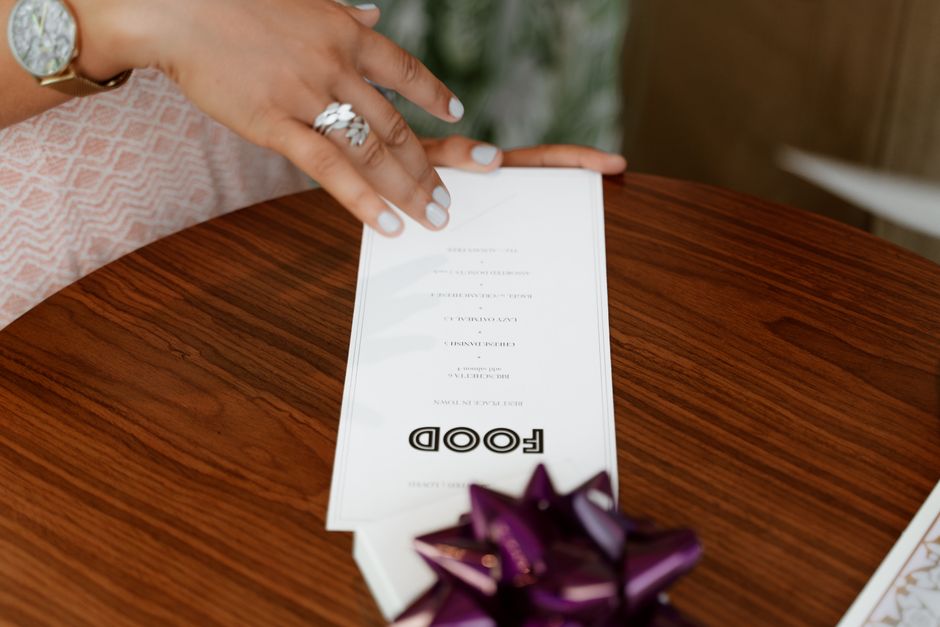 A detailed close-up of a hand holding a menu on a wooden table with elegant decor.